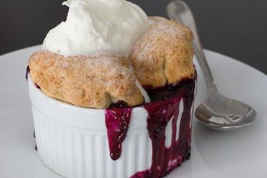 A ramekin filled with blueberry cobbler which is topped with whipped cream.