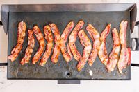 Several strips of bacon cooking on an electric griddle