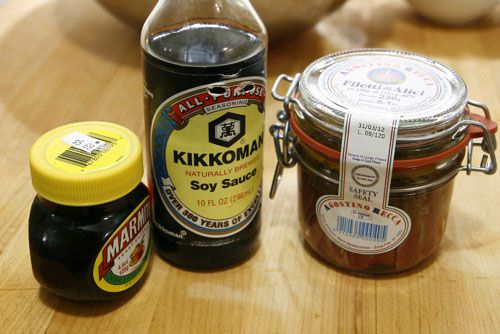 Containers of Marmite, soy sauce, and anchovies on a wooden cutting board.