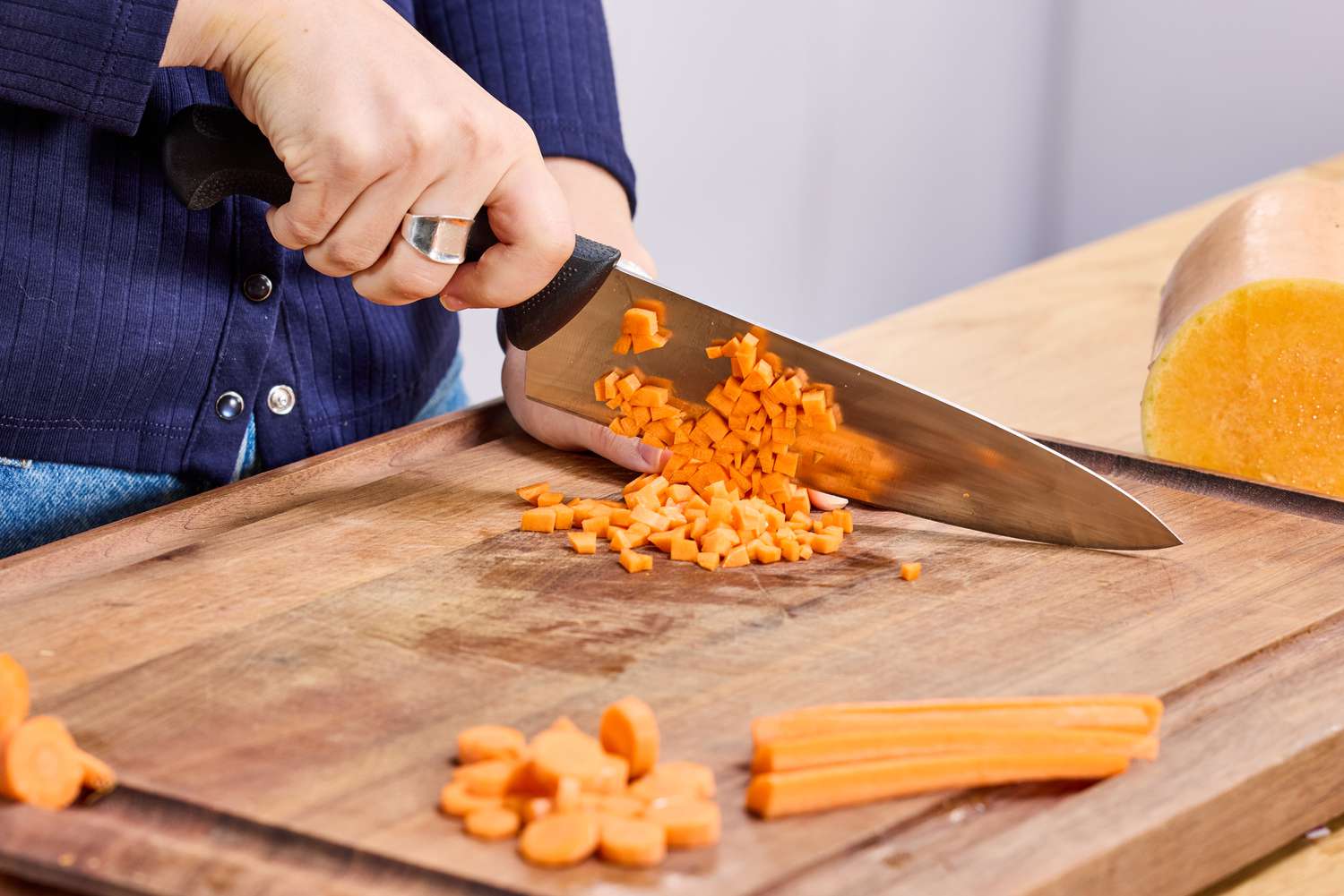 A person using the Mercer Culinary 8-Inch Millennia Chef's Knife to cut a carrot into small pieces