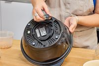 A person winds the power cord around the base of the West Bend Stir Crazy Electric Hot Oil Popcorn Popper