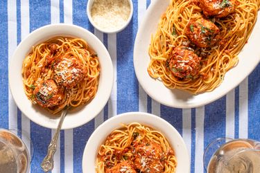 Plates of spaghetti with chicken parmesan meatballs on a blue striped tablecloth