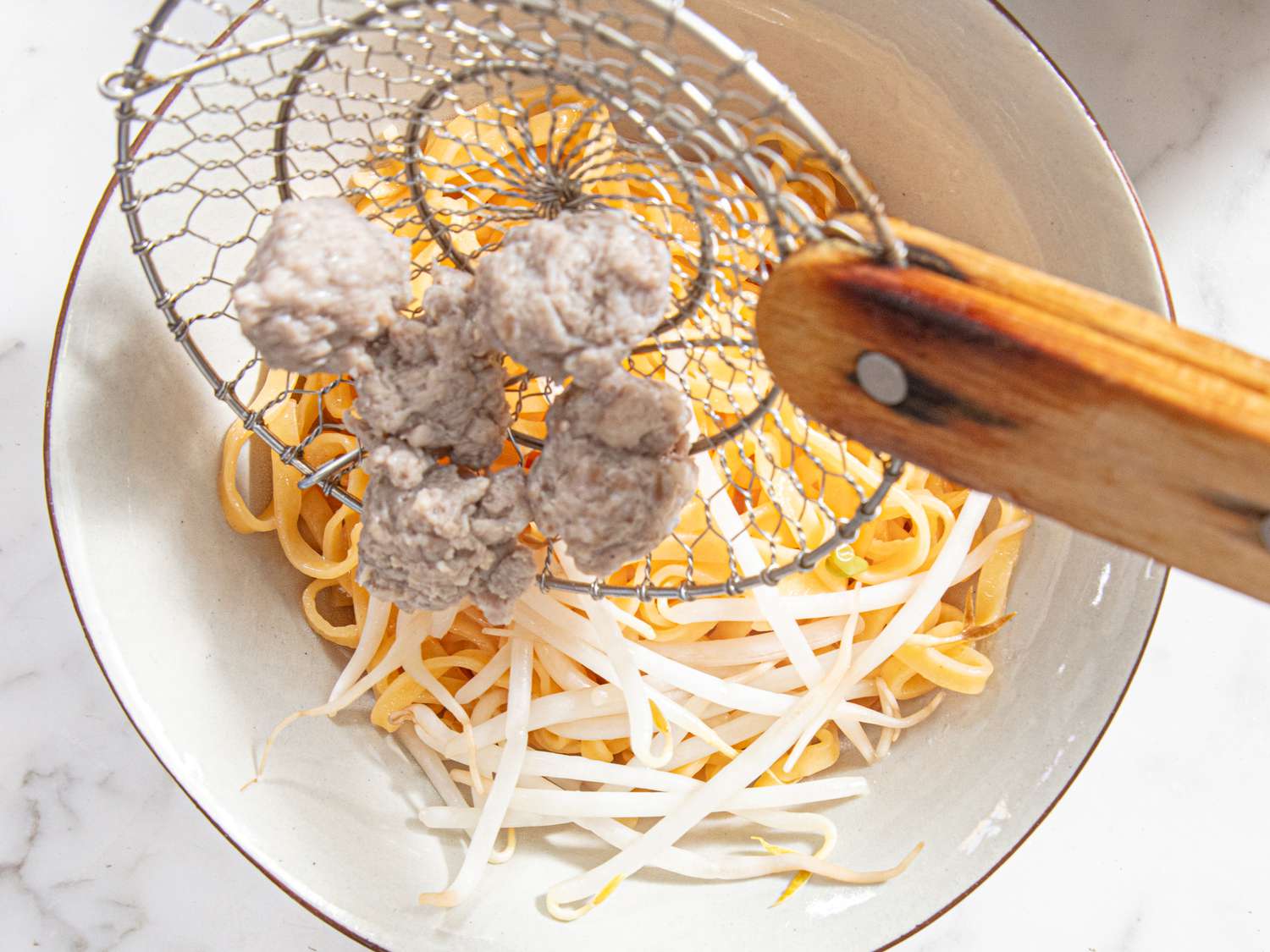 Overhead view of adding meatballs to bowl