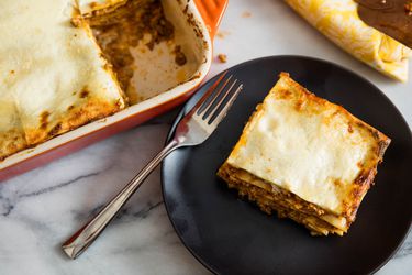 A slice of lasagna Bolognese served from a baking dish on a black plate.