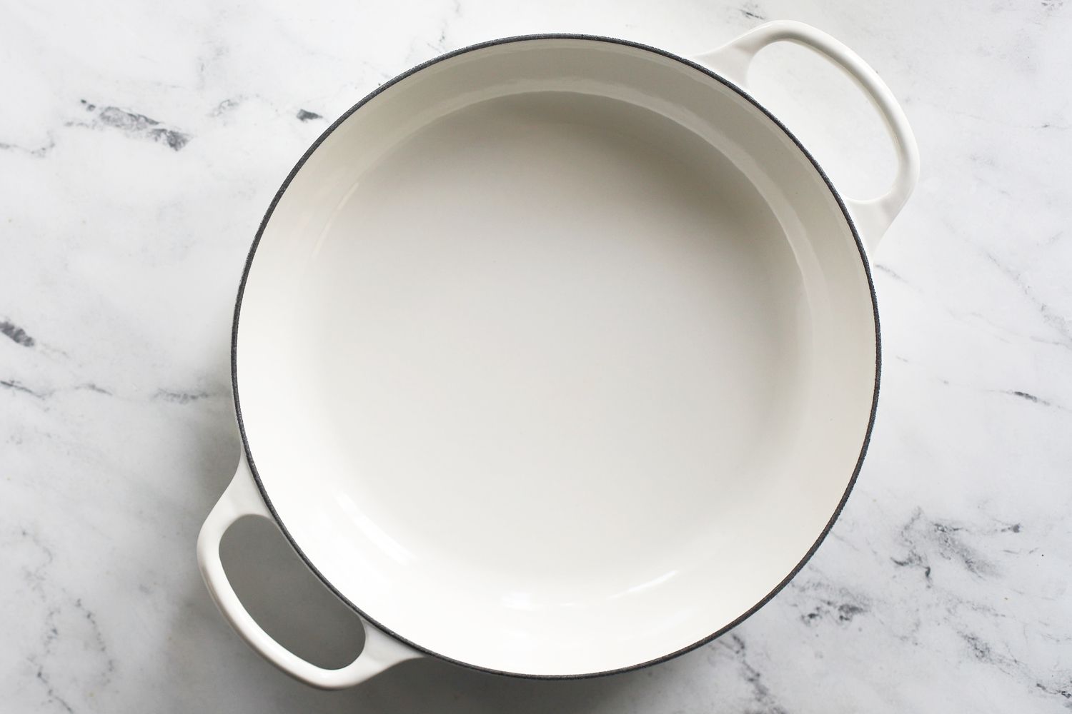 an empty white braiser with its lid off sitting on a marble surface