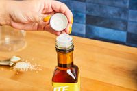 A close-up of a hand unscrewing the lid of a condiment bottle