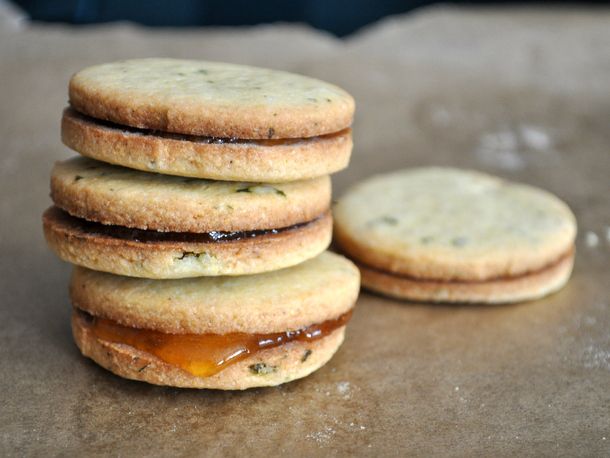 A stack of basil cornmeal sandwich cookies with apricot filling perched on a parchment-lined baking sheet.