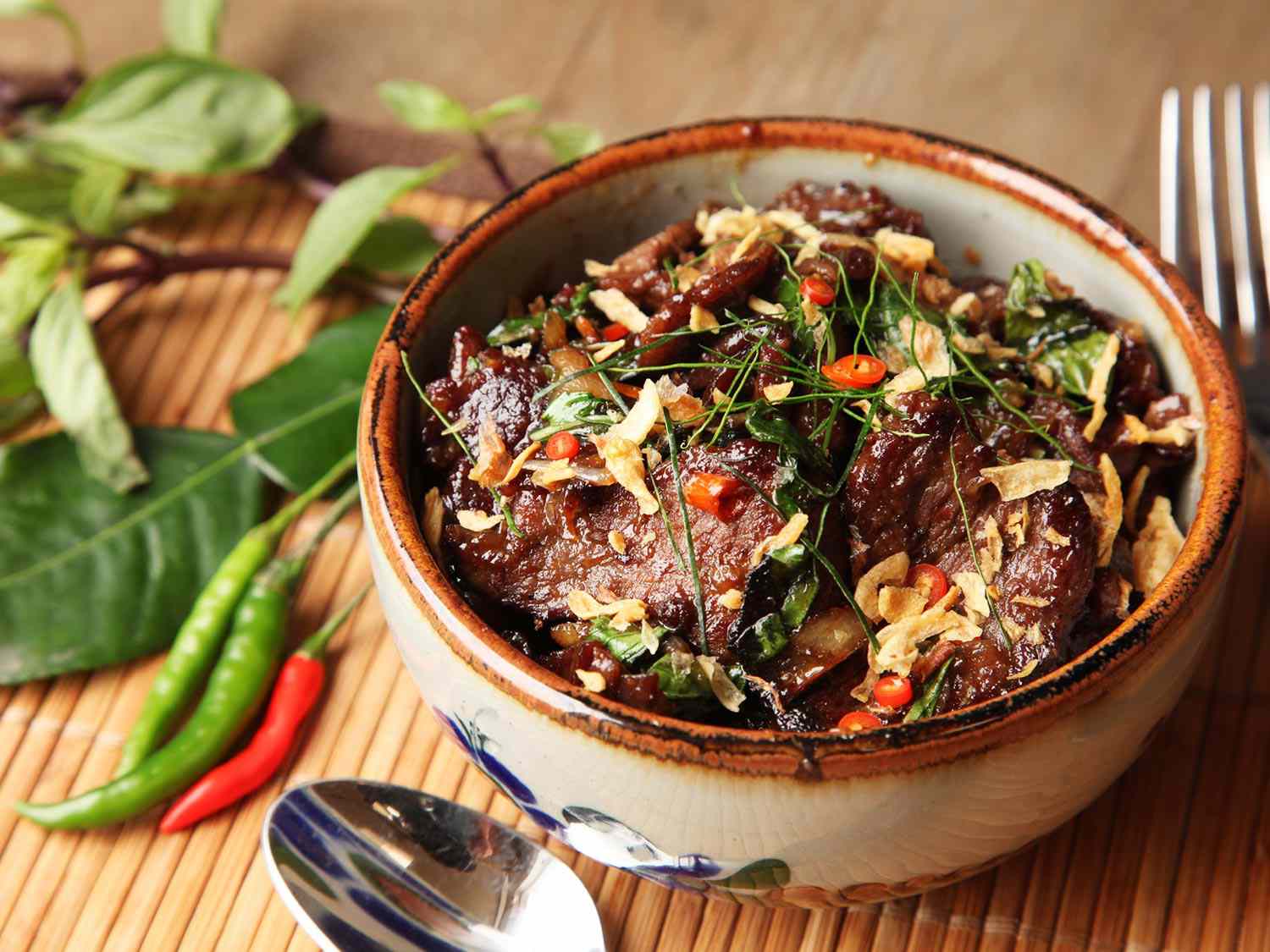 Phat bai horapha (Thai-style beef with basil and chiles), served in a bowl. Thin shreds of lemongrass, fried shallots, and chopped bird's eye chiles are scattered on the slices of well-browned beef.