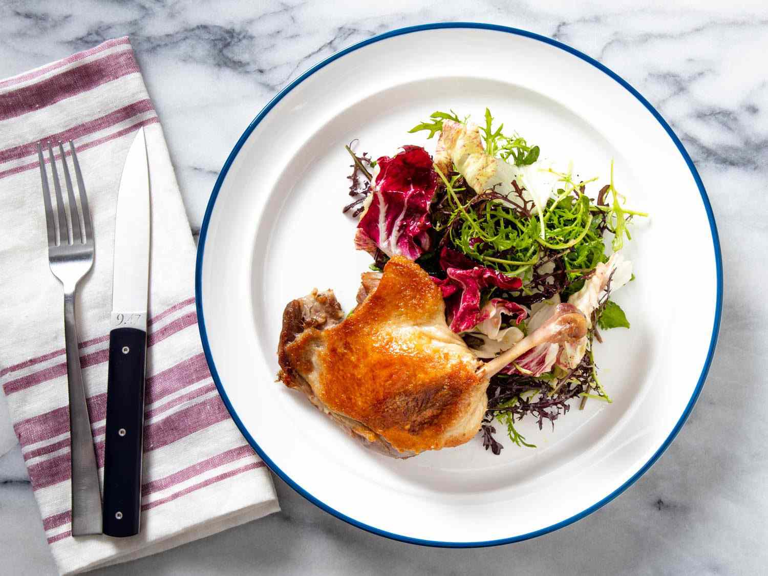 Overhead of a crisped confit duck leg with a mixed greens salad.