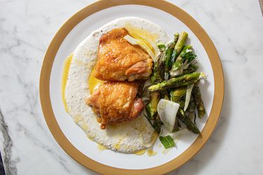 A plated dish with roasted chicken thighs, asparagus, and a creamy sauce
