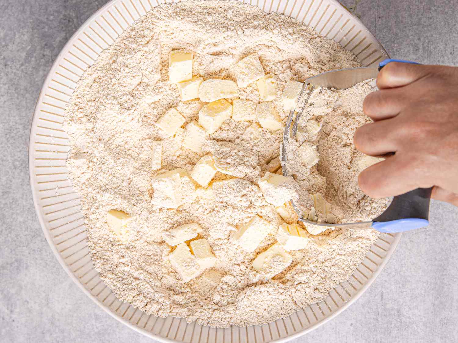 Bowl of flour with butter chunks being mixed using a pastry cutter