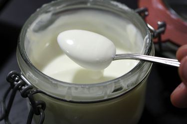 A jar of homemade crème fraîche, with a spoon dipping in it.