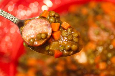 A spoonful of cotechino con lenticchie is held up to the camera.