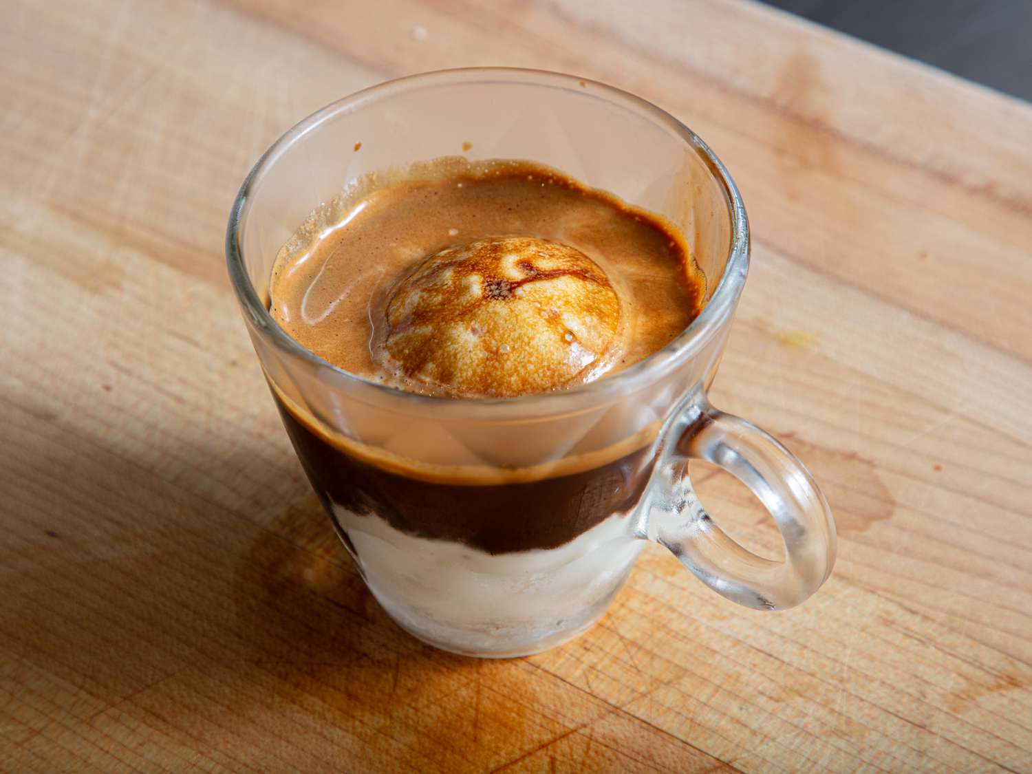 A transparent glass cup containing affogato, an espresso-based dessert with a scoop of vanilla ice cream