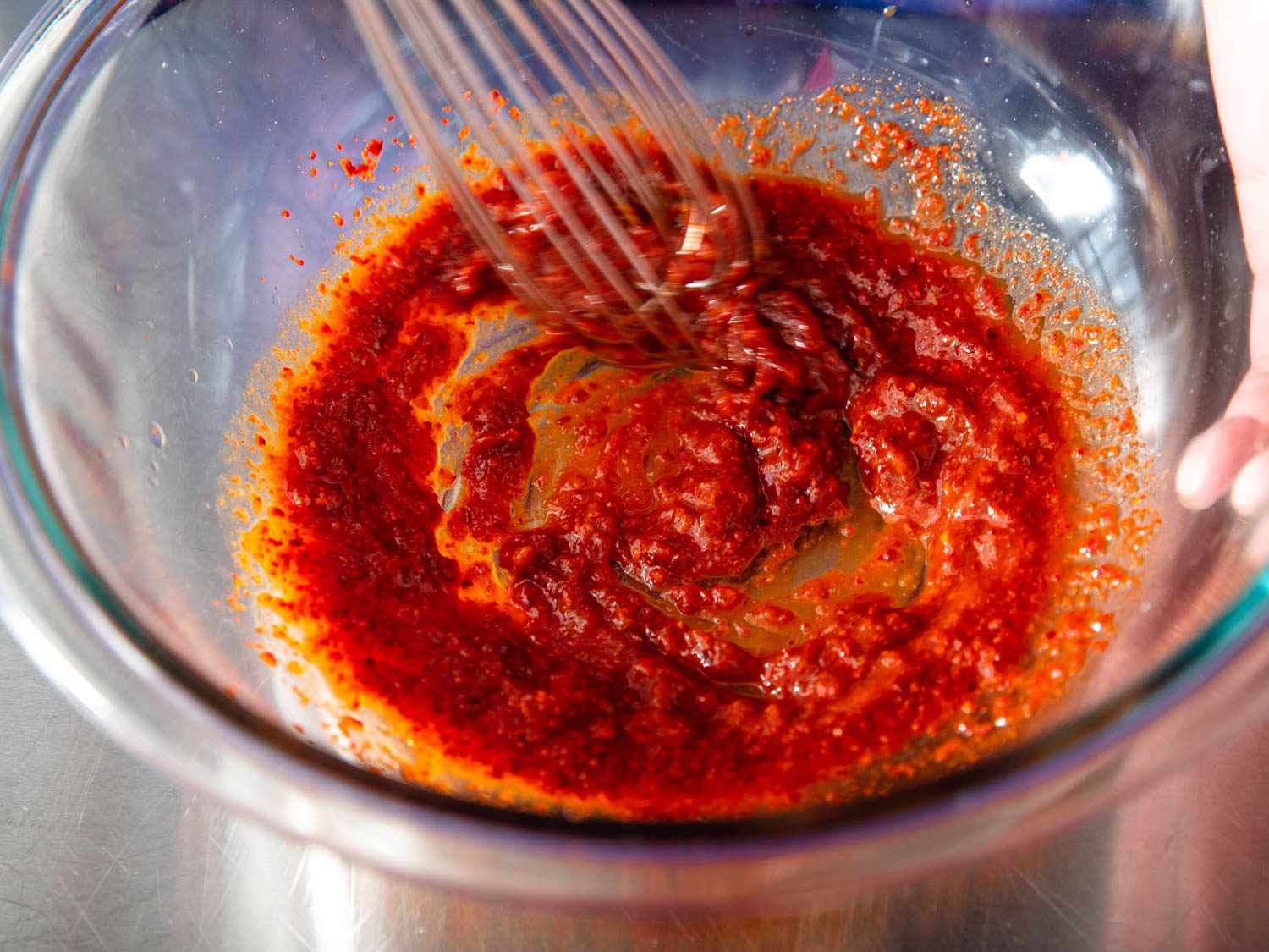 Water, soy sauce, and fish sauce are whisked together in a mixing bowl with gochugaru, gochujang, and garlic.