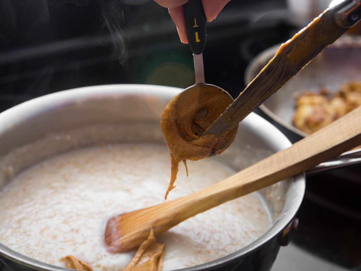 A tablespoon full of peanut butter is scraped into the cooked oats.