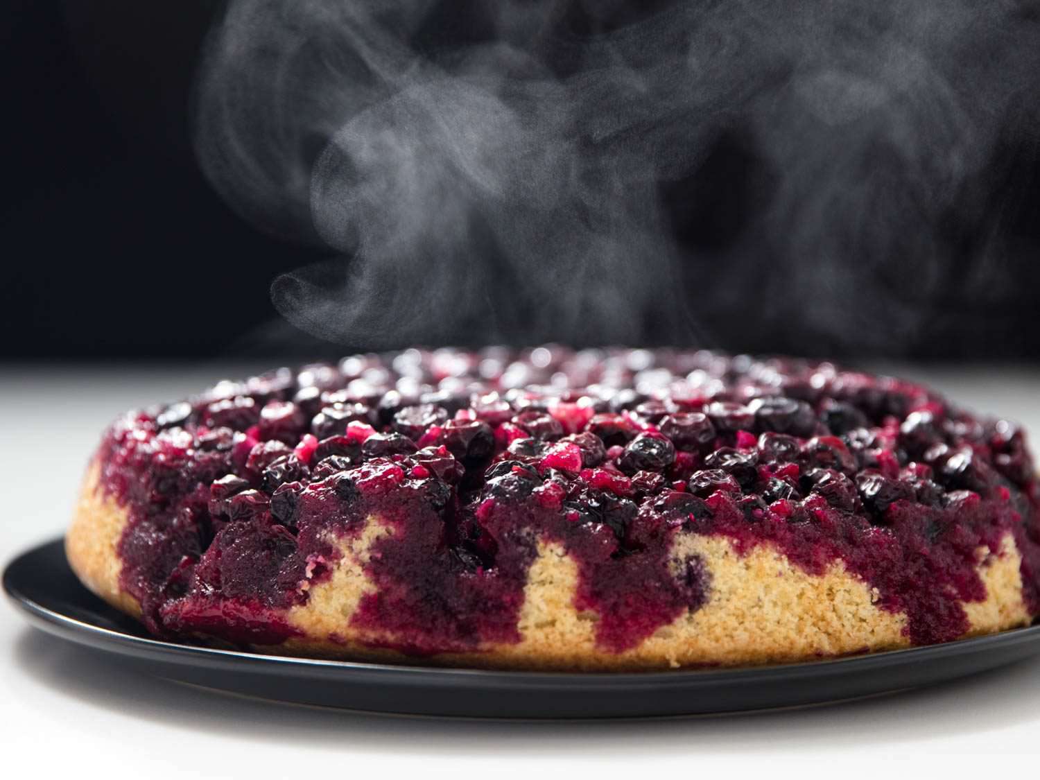 Profile view of the unmolded upside-down muffin. Steam rises from the warm, jammy berries.