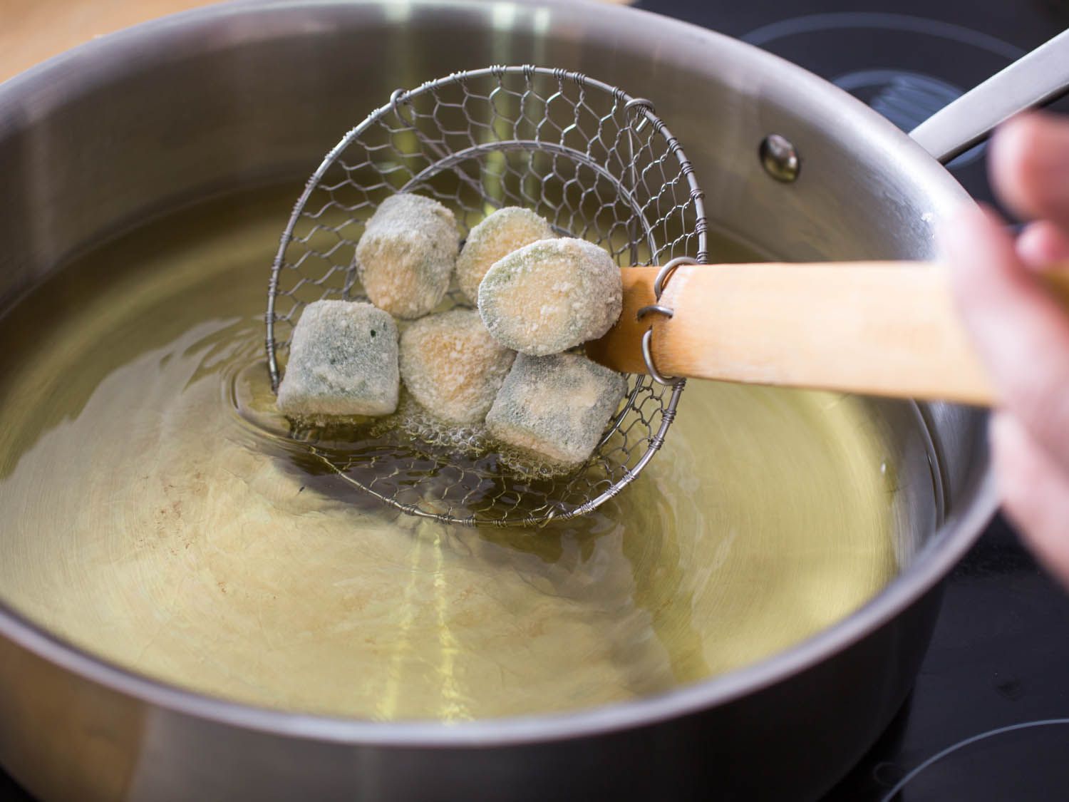 Half a dozen coated poppers are lowered into frying oil with a spider.