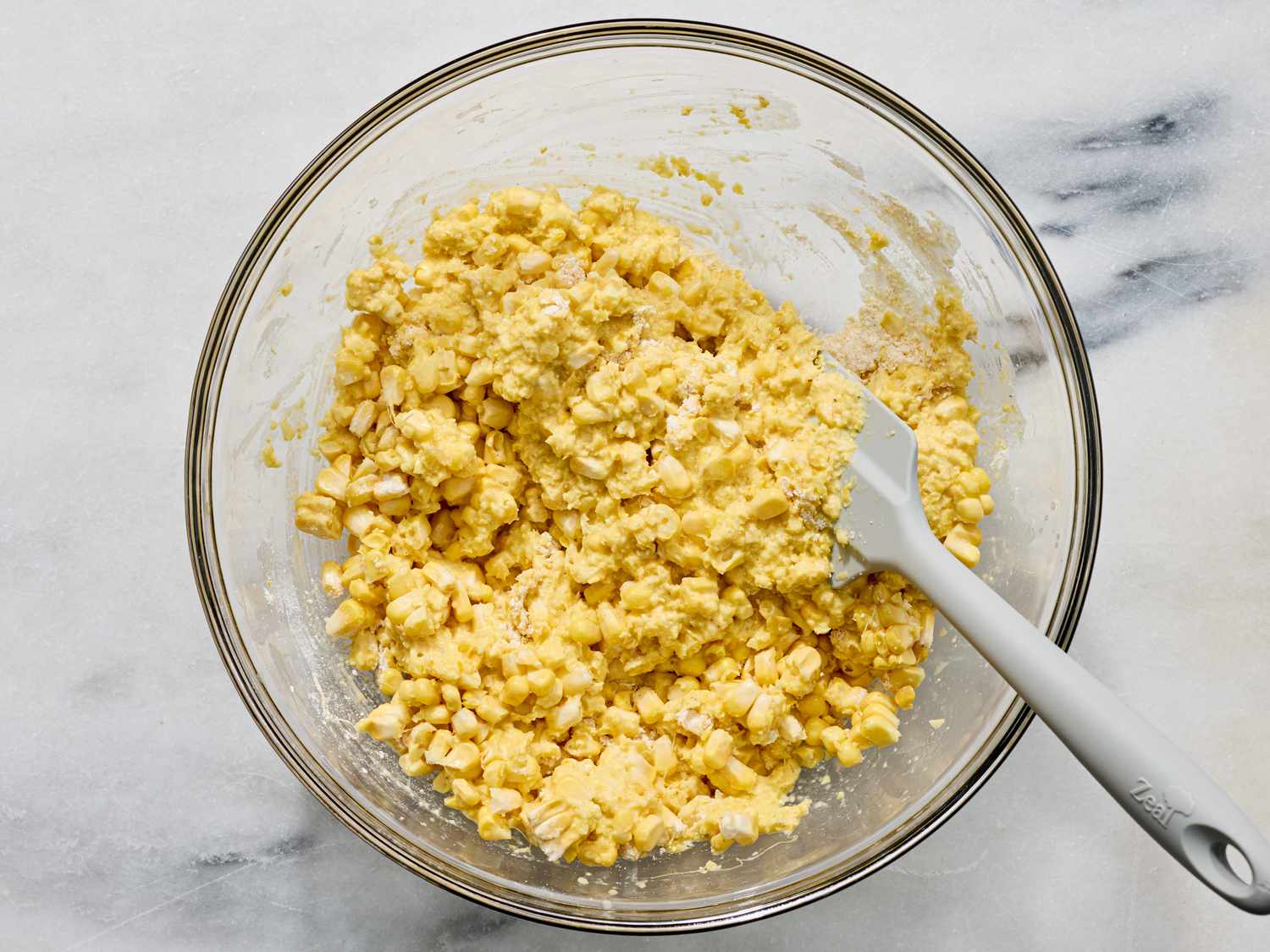 Glass bowl containing a corn mixture being stirred with a spatula