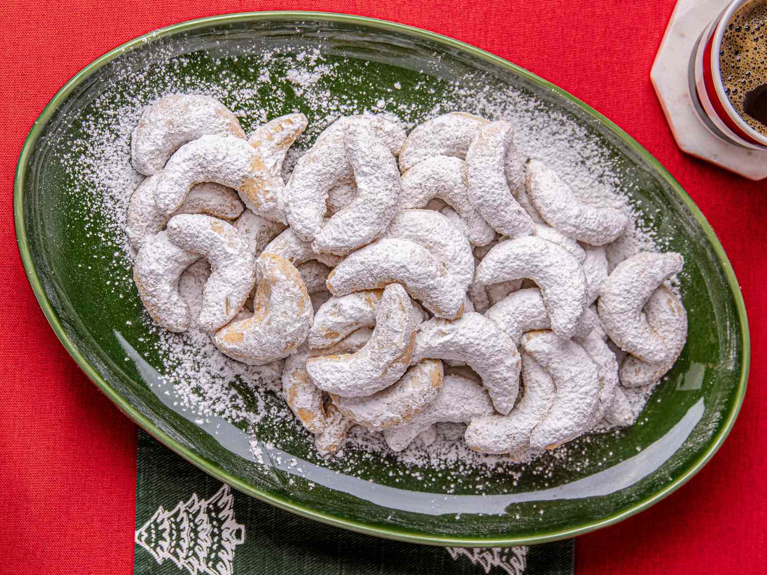 Vanillekipferl cookies arranged on a green plate dusted with powdered sugar placed on a festive table setting