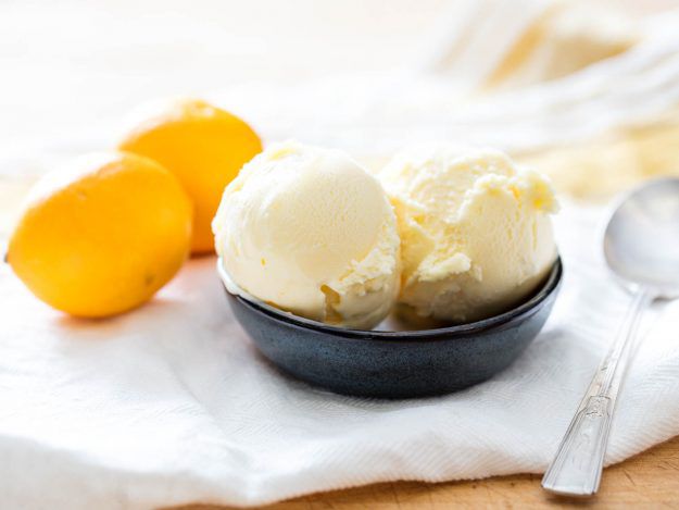 Two scoops of Meyer lemon ice cream next to two whole Meyer lemons.
