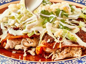 A plate of enchiladas topped with sauce cheese and fresh herbs with sauce being poured over