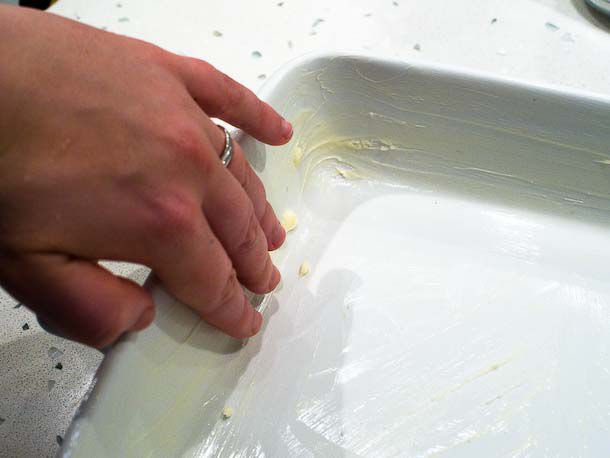A hand greasing a baking dish.