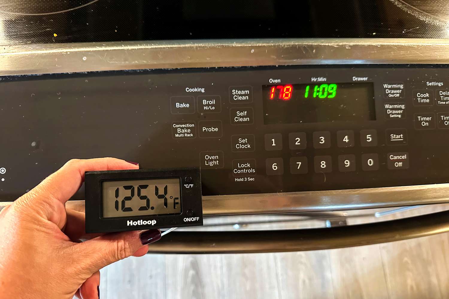 A hand holding a Hotloop thermometer showing 1254F in front of an oven panel