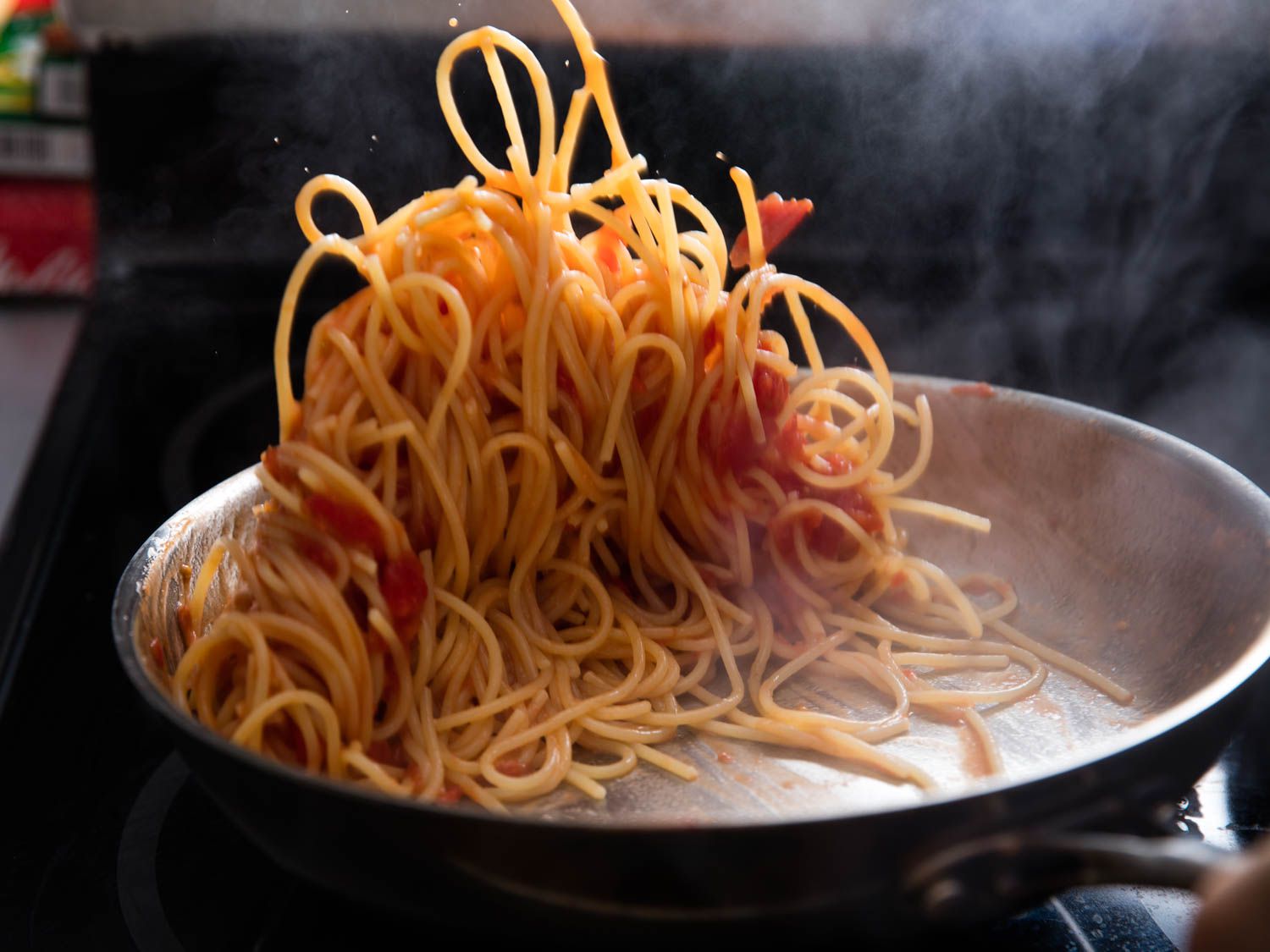 Pasta and sauce being flipped and mixed in the skillet pan.