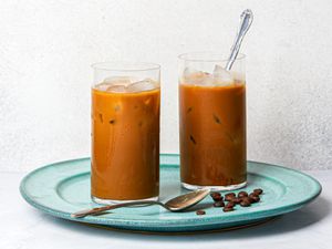 Two glasses of Vietnamese iced coffee on a blue plate with coffee beans.