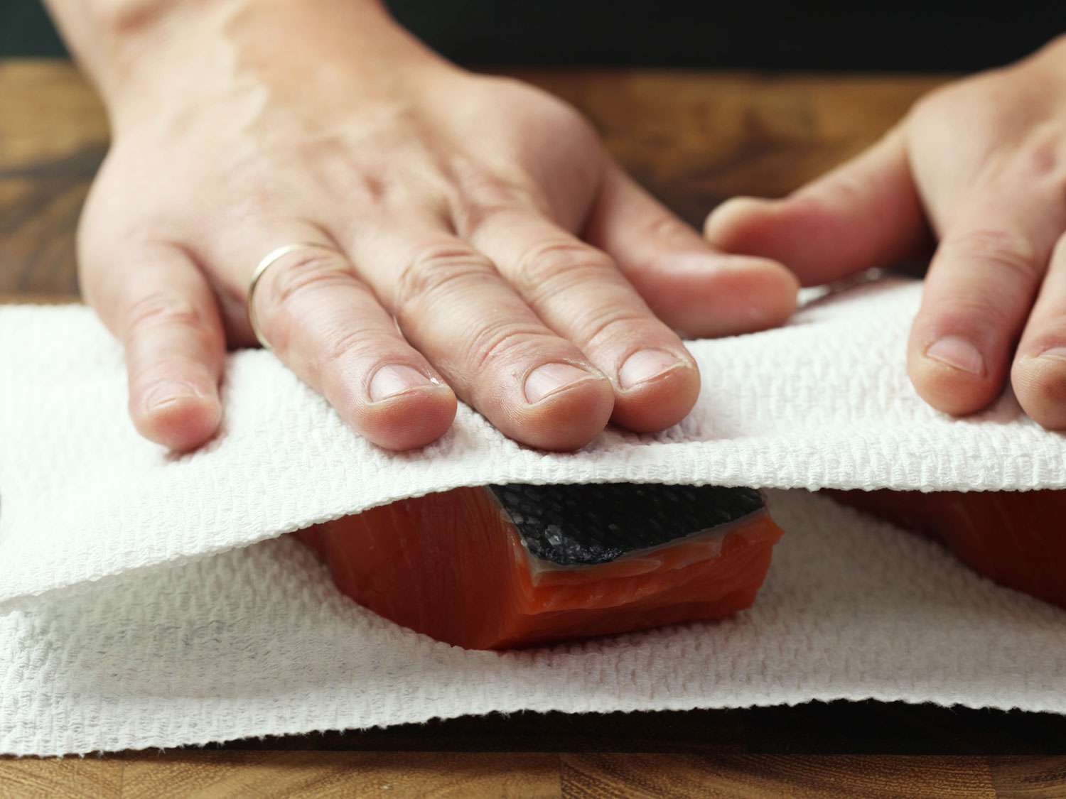 Patting raw, skin-on salmon fillet dry using paper towels on the top and bottom of the fillet.