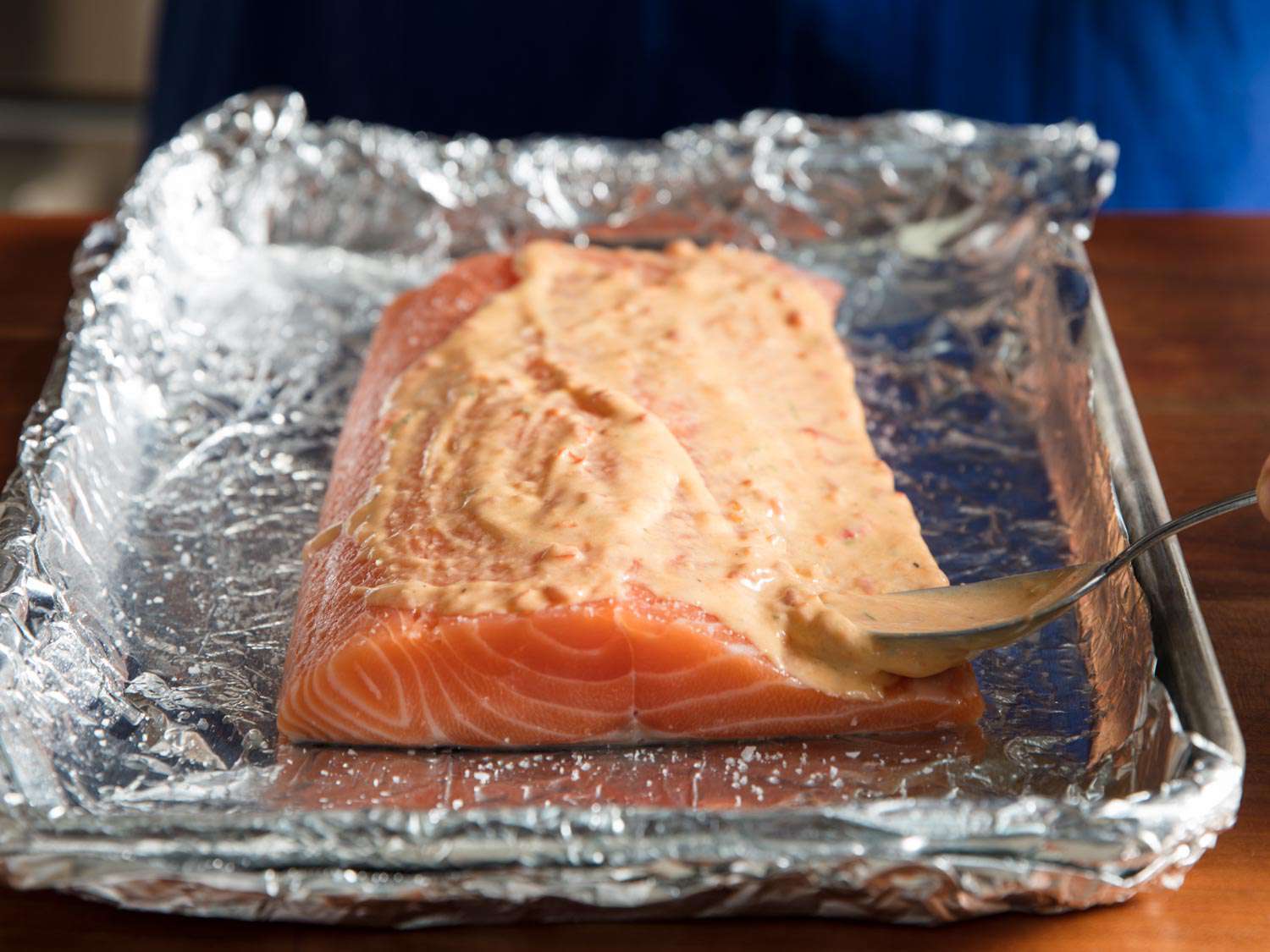 The salmon fillet is placed on a foil-lined baking sheet and coated with harissa mayo.