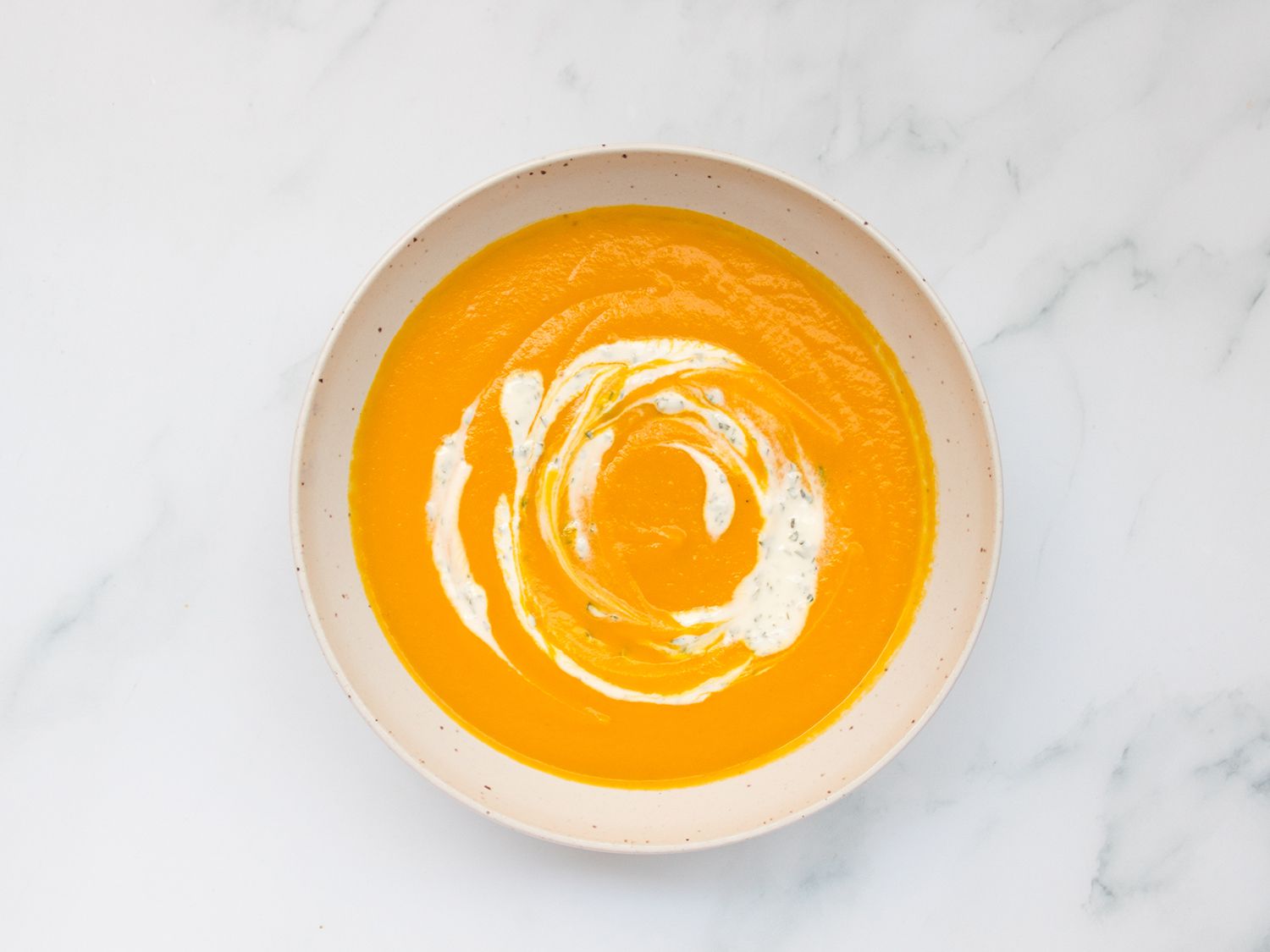 Carrot soup and yogurt sauce in a white bowl.