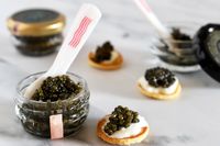 A jar of osetra caviar from The Caviar Co next to a blini topped with crème fraîche and a scoop of caviar