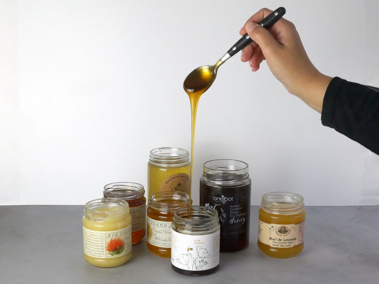 a hand pulling a drip of honey from a jar