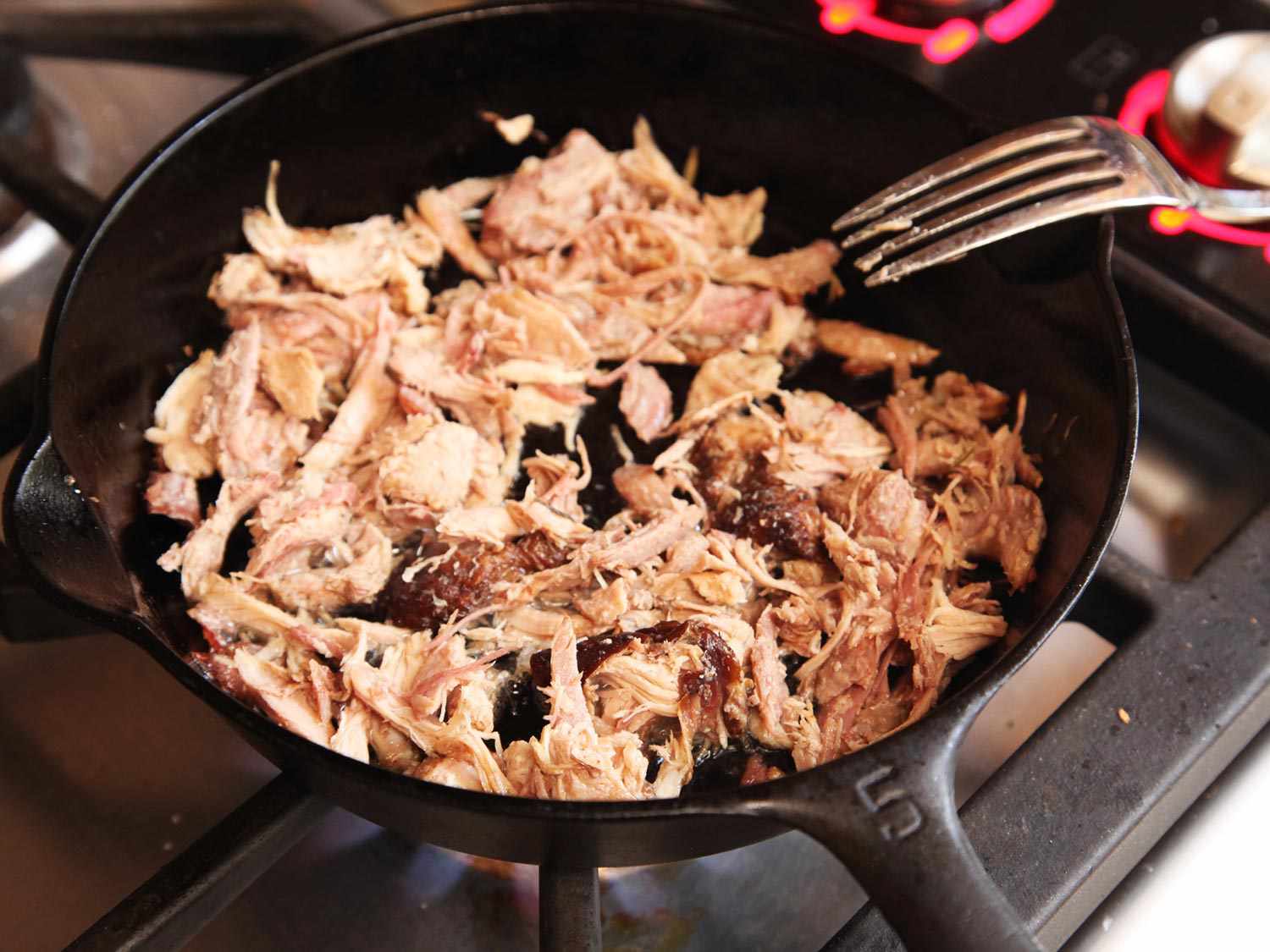 Frying shredded turkey in a cast iron skillet on a stovetop.