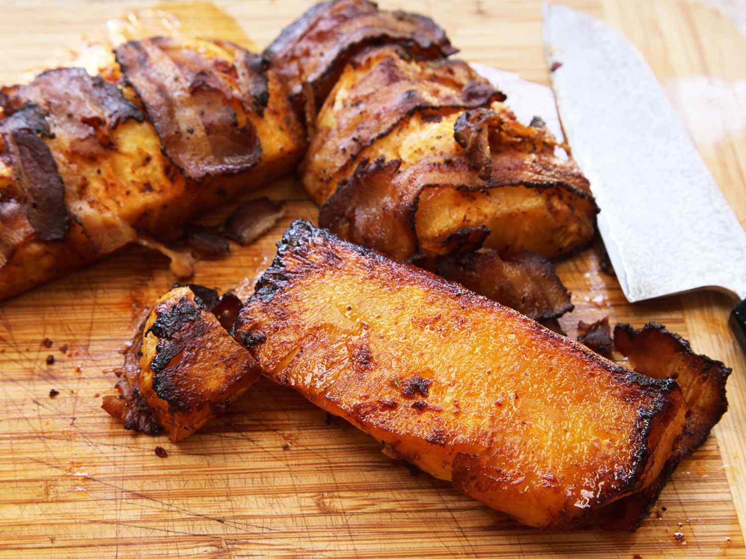 A closeup of the roasted, bacon-wrapped pineapple on a cutting board, fresh from the oven.