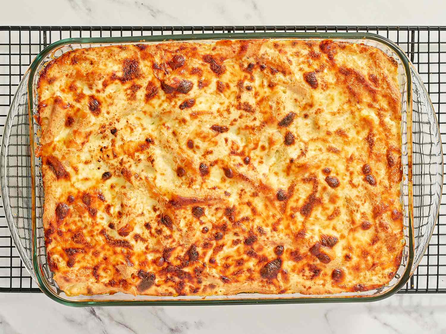 A baked lasagna in a rectangular glass dish resting on a cooling rack