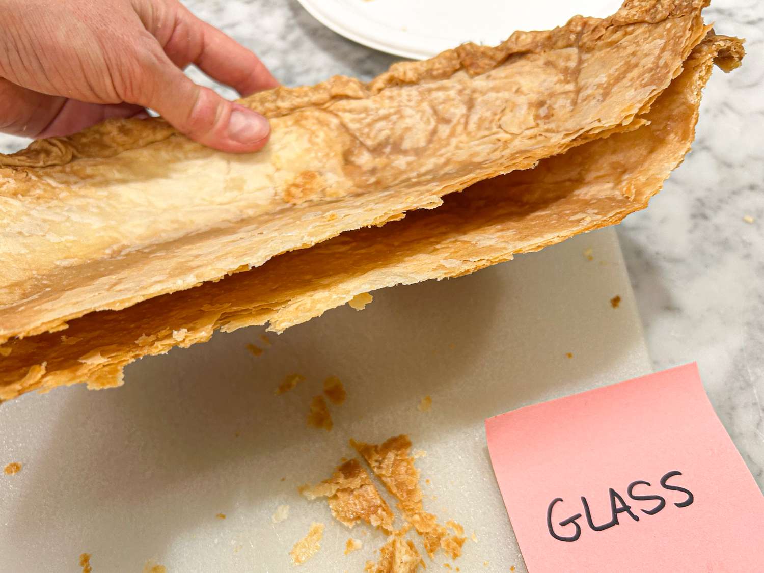 A hand holding a broken pie crust labeled Glass on a sticky note nearby