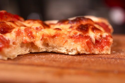 Close-up of New York-style pizza with a bite taken out so you can see the structure of the crust.