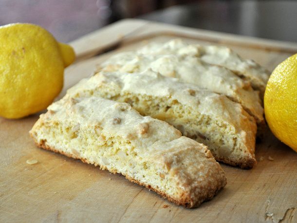 Closeup of lemon pine nut biscotti on a cutting board, flanked by two lemons.