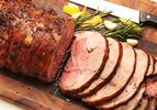 A slow-roasted leg of lamb sliced on a cutting board, flanked by rosemary sprigs, peeled garlic cloves, and wedges of lemon.