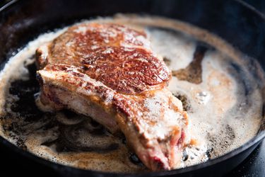 A bone in steak cooking in a cast iron skillet. 