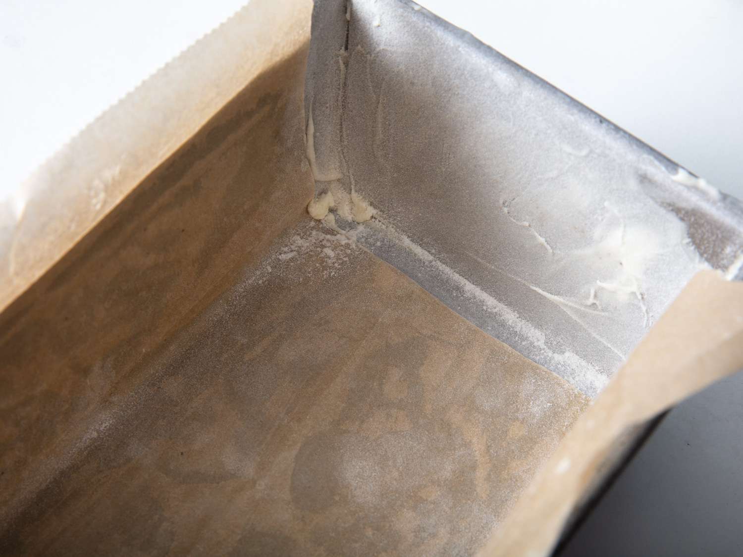 A loaf pan that's been prepared with butter, parchment, and flour for an apple cake.