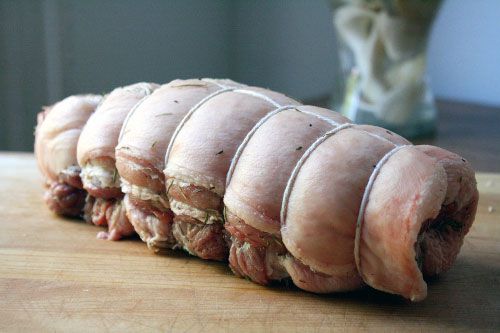 An uncooked pork brisket tied at intervals with twine.