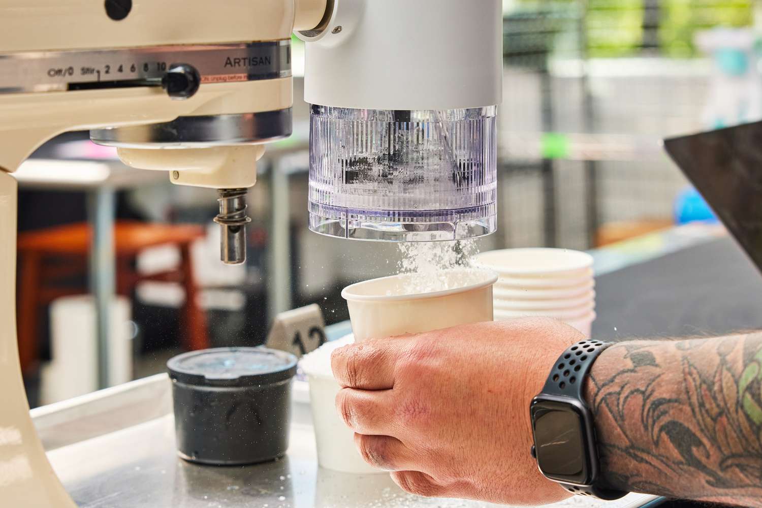 A person holding a cup underneath a shaved ice attachment and catching shaved ice in the cup