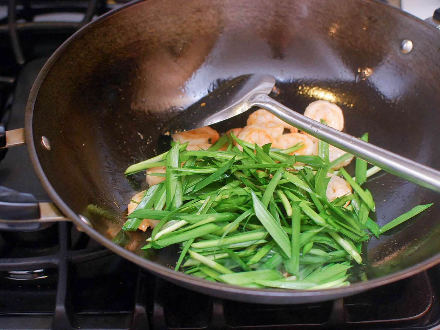 Chives being stir-fried in a wok with shrimp. 