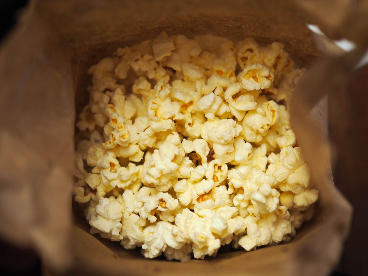 Peering down into the interior of a brown paper bag filled with popped popcorn.