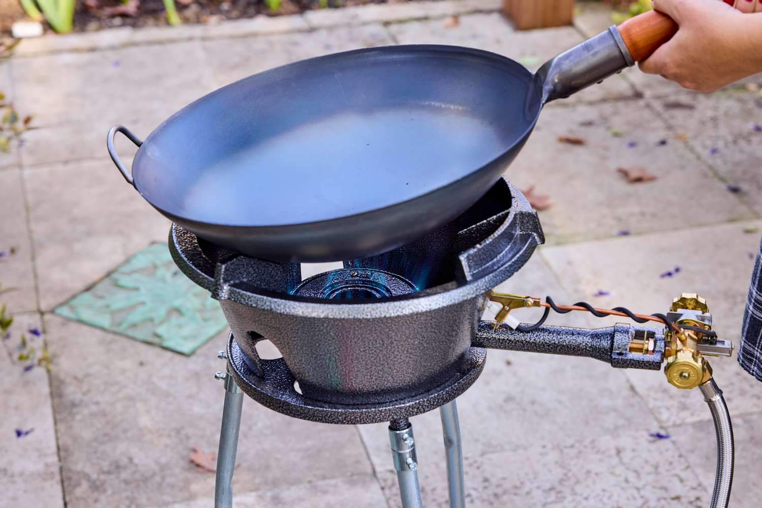 A person placing a wok onto an outdoor wok burner.