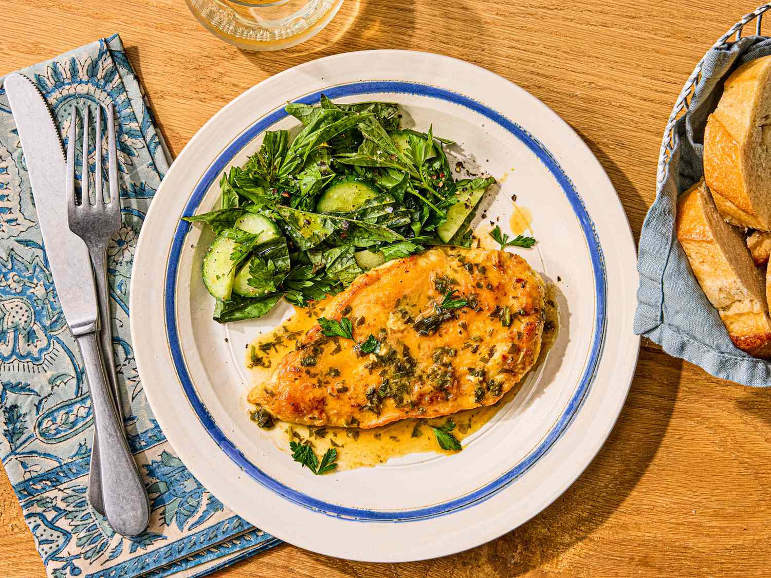 A plate with chicken paillard and a side of greens, placed on a wooden table with a fork and a napkin